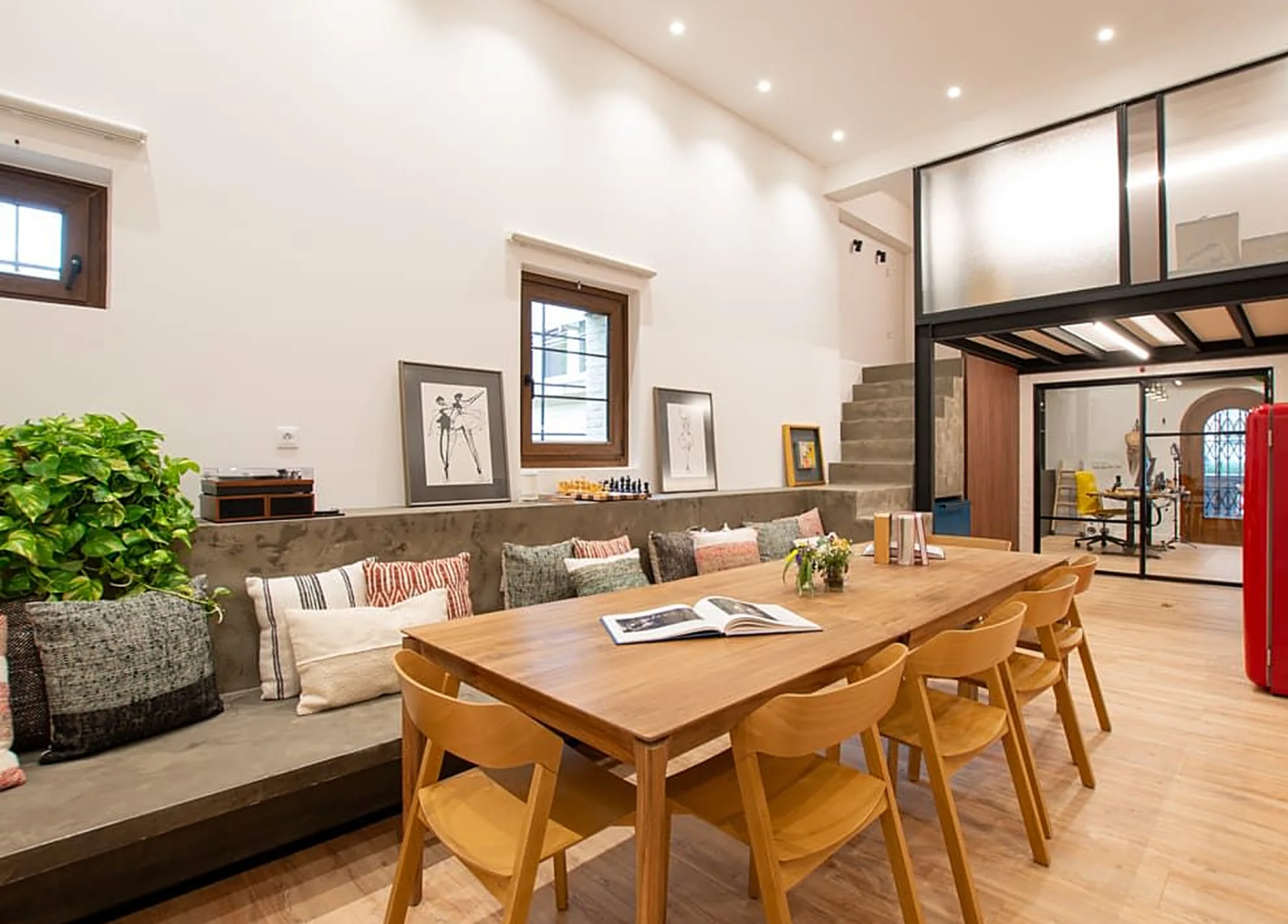 La sala de El Paréntesis: mesa larga de madera con sillas, banco corrido con cojines y la escalera al fondo